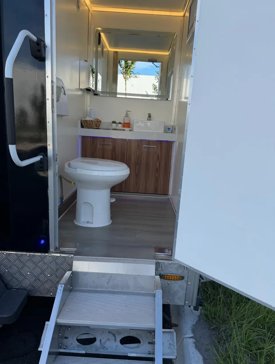 Restroom trailer interior with flushing toilet, vanity and lit mirror