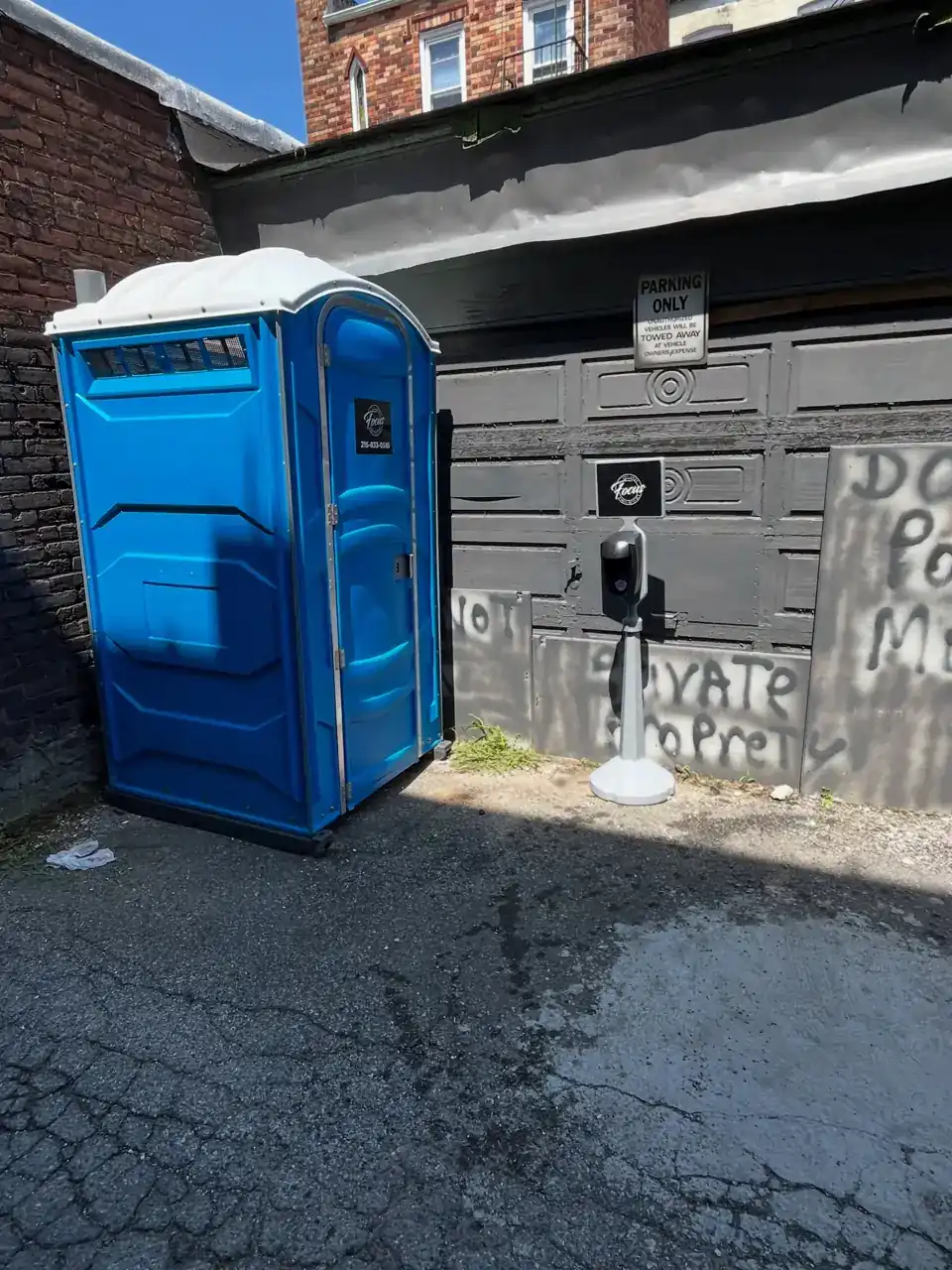 Standard blue portable toilet set beside a building on a paved driveway