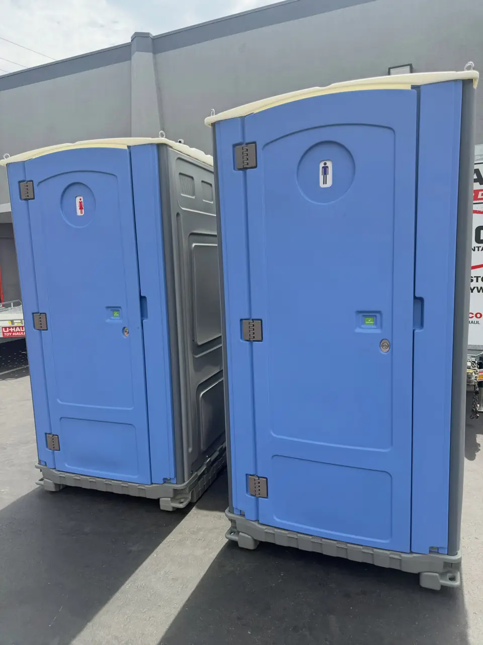 Two standard blue portable toilets placed side by side on pavement